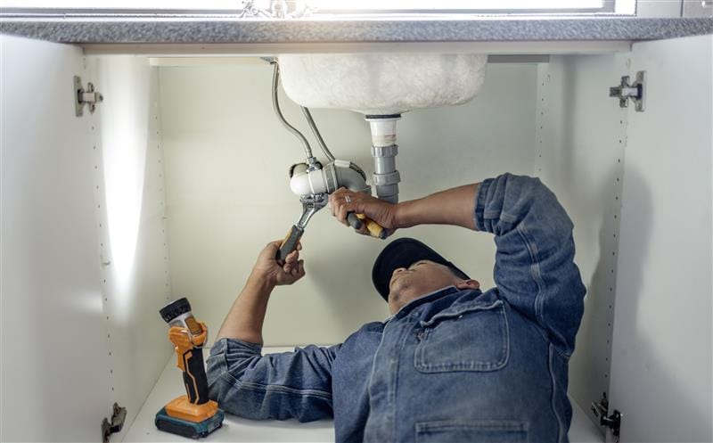 Plumber repairing pipes beneath a bathroom sink in Seminole