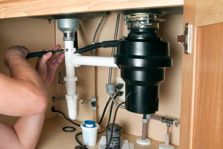 Plumber installing a garbage disposal beneath a kitchen sink in Seminole