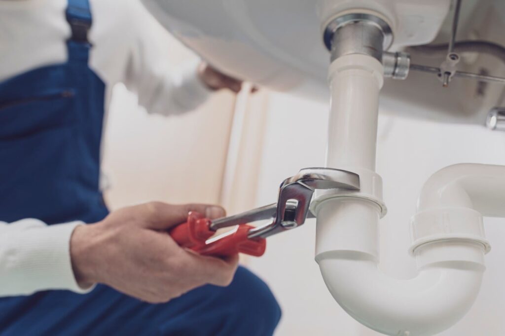 Plumber repairing a white drain pipe beneath a sink in Seminole