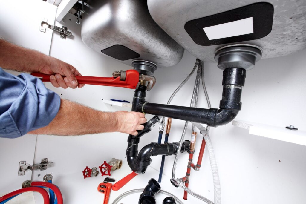 Plumber repairing drain pipes beneath a kitchen sink in Seminole